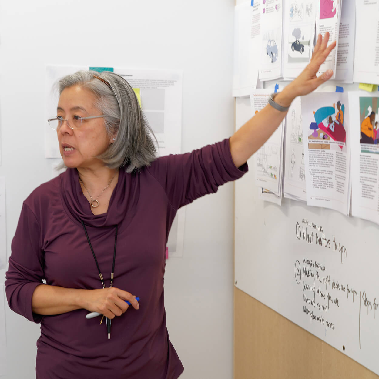 Tomoko teaching and pointing to whiteboard/wall